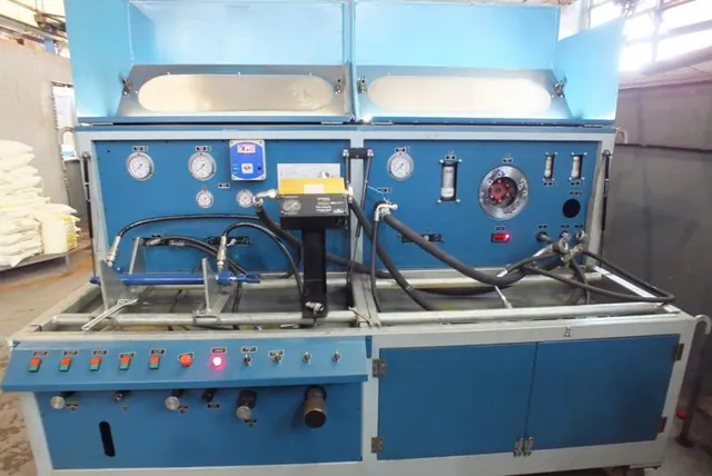 Bancada de teste hidráulico azul, com o cilindro acoplado e o painel de instrumentos à esquerda