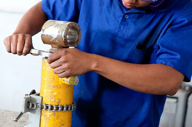 Montagem de cilindro hidráulico: operador de uniforme azul encaixando a camisa na bancada