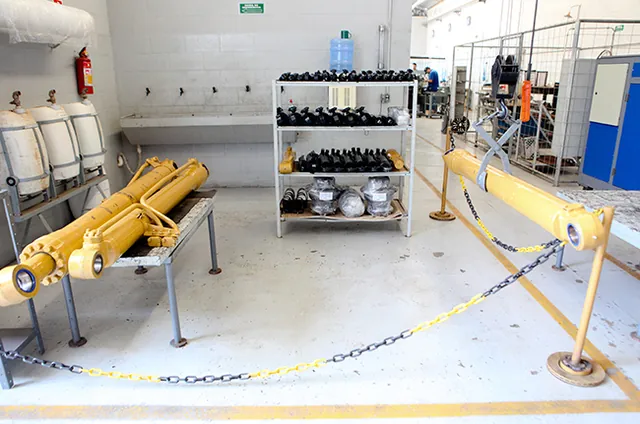 Cilindros hidráulicos montados no cavalete da oficina, com as prateleiras de componentes ao fundo