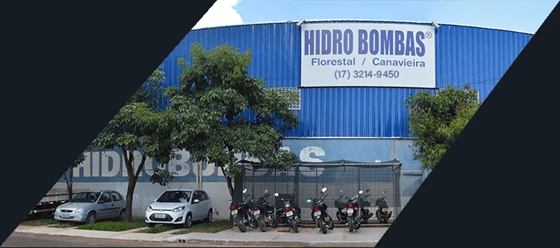 Frente da sede vista da rua, com a placa HIDRO BOMBAS sobre o portão e motos estacionadas sob as árvores