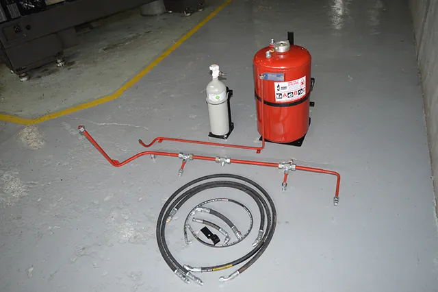 Conjunto do kit anti-incêndio disposto no chão da oficina: reservatório vermelho, ampola de nitrogênio, tubos curvados e flexíveis
