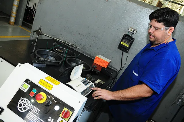 Operador de uniforme azul no painel da lapidadora, acompanhando a medição de rugosidade