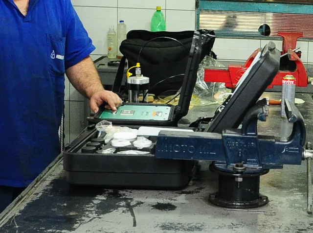 Técnico de uniforme azul operando o medidor de partículas acoplado ao equipamento